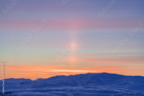 Very beautiful sunset at Scandinavian mountains - red orange sun beams coloring the white snow and blue sky