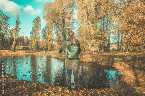 autumn forest landscape, a girl with a backpack feeds ducks at the lake