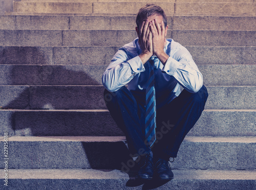 Depressed sad business man in total despair felling hopeless and frustrated sitting in city stairs photo