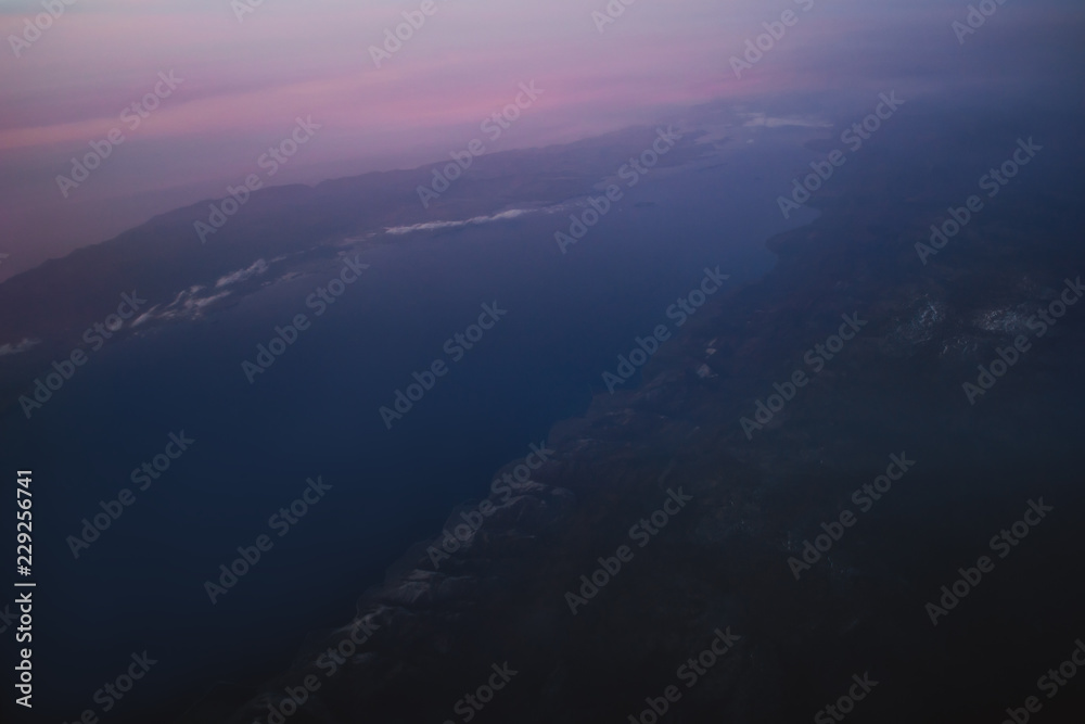 view of the earth and Lake Baikal from the window of an airplane from a height of 10,000 meters above the clouds illuminated by the rays of the rising sun
