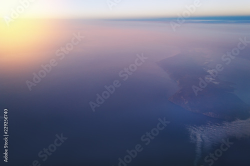 view of the earth and Lake Baikal from the window of an airplane from a height of 10,000 meters above the clouds illuminated by the rays of the rising sun