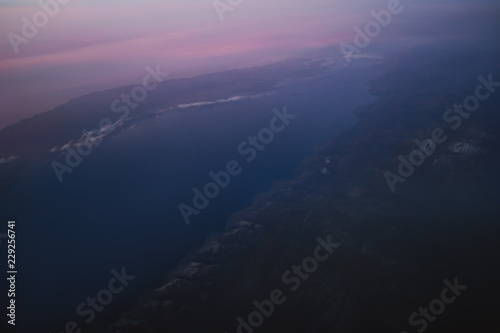 view of the earth and Lake Baikal from the window of an airplane from a height of 10,000 meters above the clouds illuminated by the rays of the rising sun