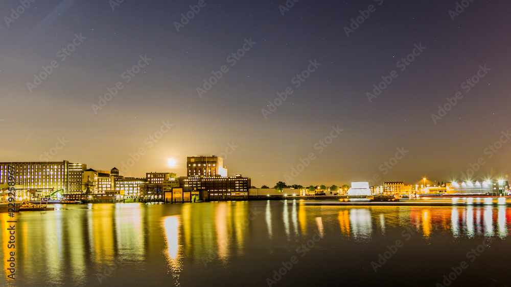 Night view of buildings on the shore of new Maas in business city of Rotterdam, yellow lights reflected on water surface, calm night in South Holland in the Netherlands. Long exposure photography
