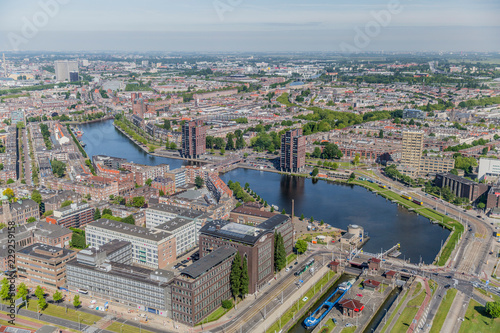 Aerial cityscape of Rotterdam with its buildings, canal, bridges, boats and small green areas, sunny day with a grayish sky with the horizon in the background in South Holland, Netherlands