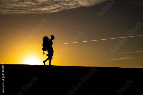 Silhouette of a young man with hiking backpack walking across the dunes of Maspalomas in Gran Canaria during sunset