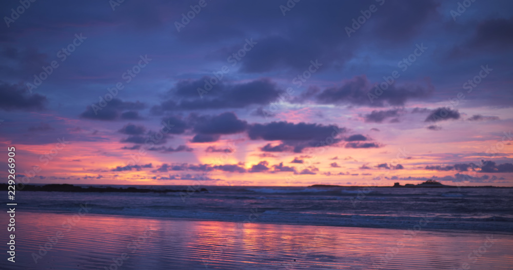 Out of focus background plate of orange, purple and blue sunset on the beach