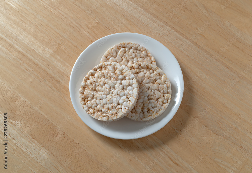 Top view of three multigrain rice cakes on a white plate atop a wood table. Top view of three multigrain rice cakes on a white plate atop a wood table.