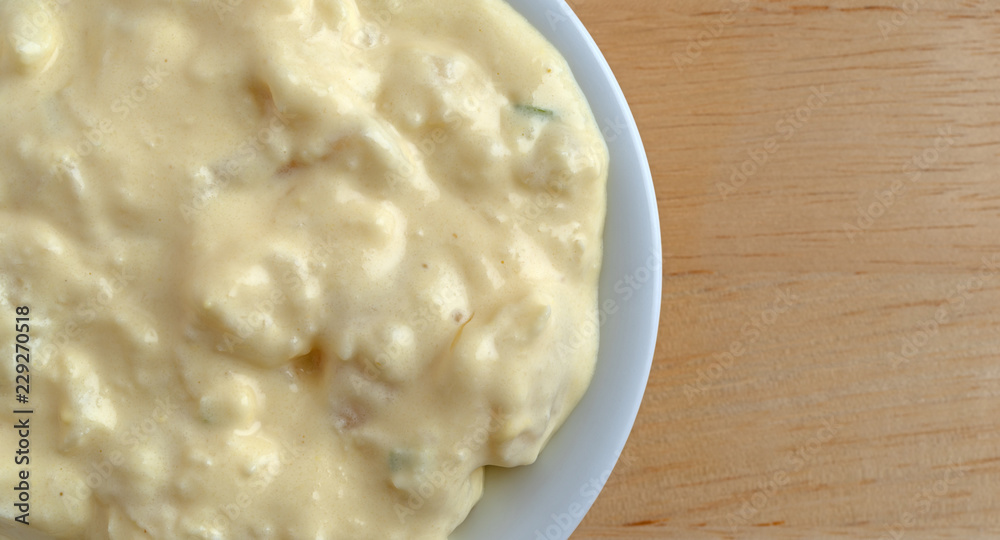 Top close view of a portion of potato and egg salad in a small bowl on a wood table. Top close view of a portion of potato and egg salad in a small bowl on a wood table.