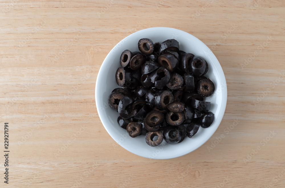 Top view of a white bowl filled with sliced olives on a wood table. Top view of a white bowl filled with sliced olives on a wood table.