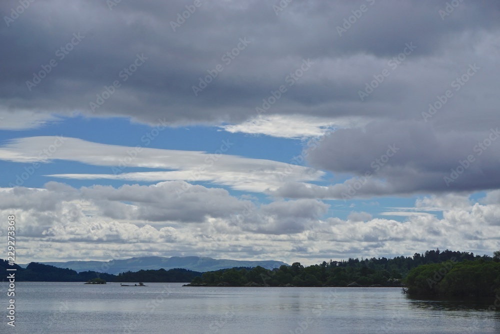 Luss, Scotland: View of Loch Lomond, with mountains in the distance, under a blue sky with white clouds. Loch Lomond is part of the Loch Lomond and The Trossachs National Park, established in 2002.