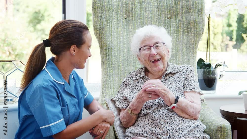 Senior Woman Sitting In Chair And Talking With Nurse In Retirement Home