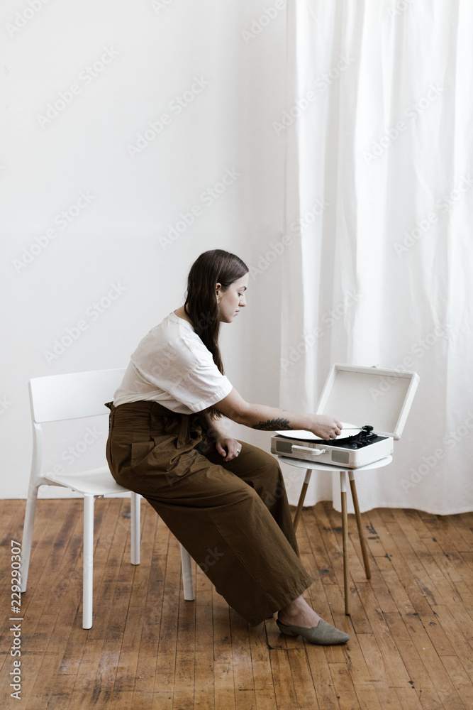stylish young woman putting a record on in a minimal white interior stylish young woman putting a record on in a minimal white interior