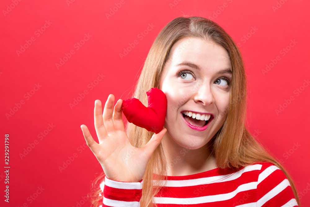 Happy young woman holding a heart cushion on a red background Happy young woman holding a heart cushion on a red background