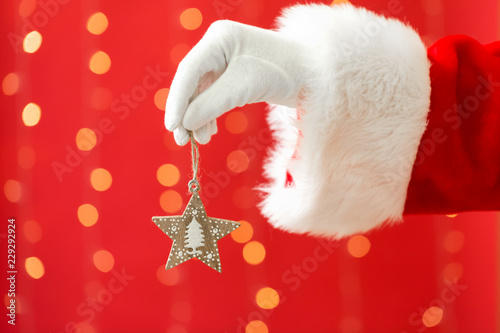 Santa holding a star ornament on a shiny light red background