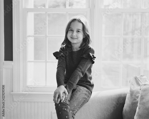 Black and white portrait of a beautiful young girl sitting on the armrest of a chair photo