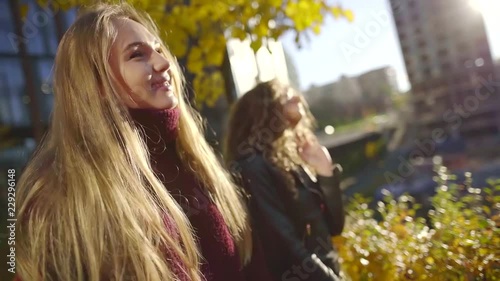 carefree blonde sisters are dancing and singing outdoors in autumn city garden in sunny day photo