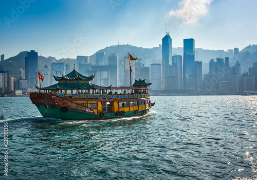 Passenger boat carrying tourists between the Islands of Hong Kong with modern skyscrapers in the background 
