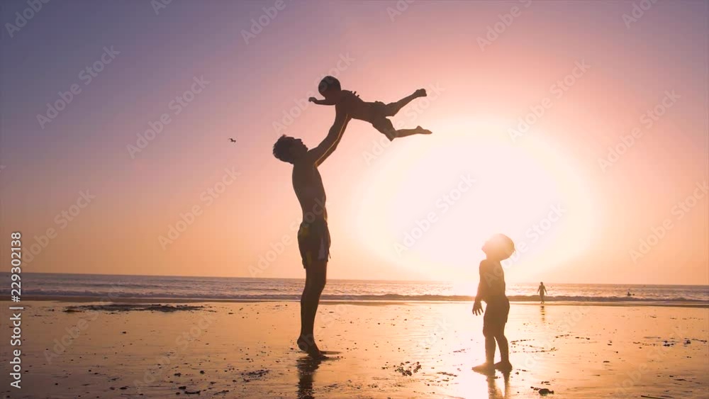 Ultra slow motion - silhouette of father and son playing together in the beach at sunset Ultra slow motion - silhouette of father and son playing together in the beach at sunset