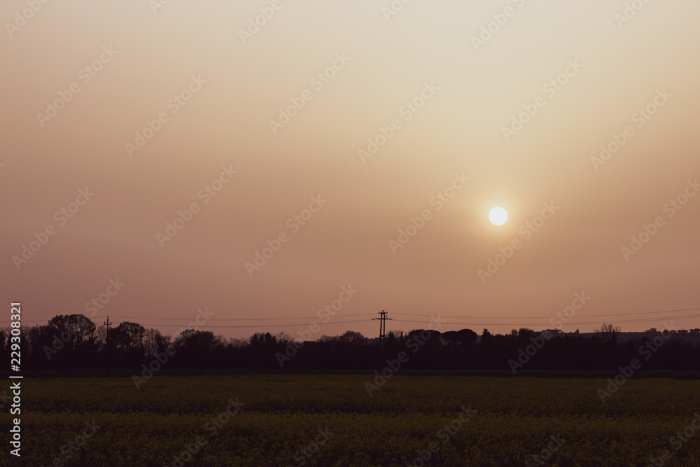 Sunset with sand suspended in the atmosphere, coluring the sky red, over some fields and hills Sunset with sand suspended in the atmosphere, coluring the sky red, over some fields and hills