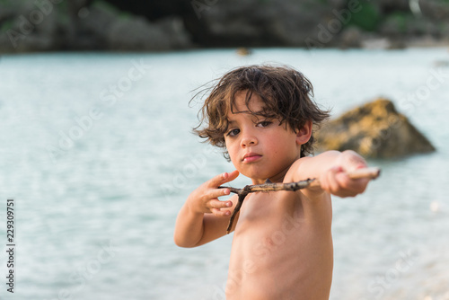 young boy child by the beach playing with a found stick photo