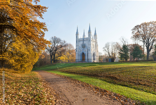 Catholic chapel among autumn nature, path with fallen leaves, trees with yellow foliage