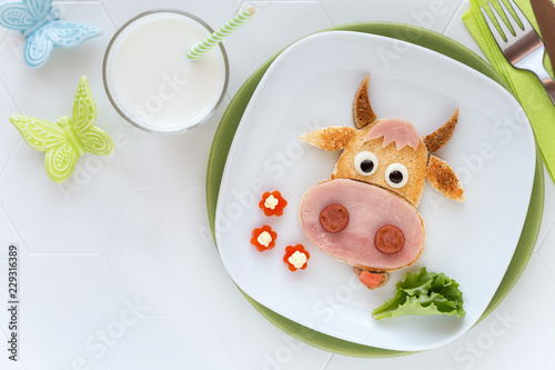 Fun food for kids - cute cow shaped sandwich with ham sausages served with a glass of milk for breakfast or dinner