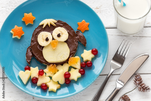 Fun food for kids - Cute penguin shaped toast with a chocolate spread garnished with fresh fruits and berries for breakfast on a blue plate with festive Christmas decorations