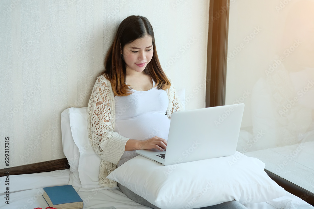 Pregnant woman is using laptop computer on bed. Pregnant woman is using laptop computer on bed.