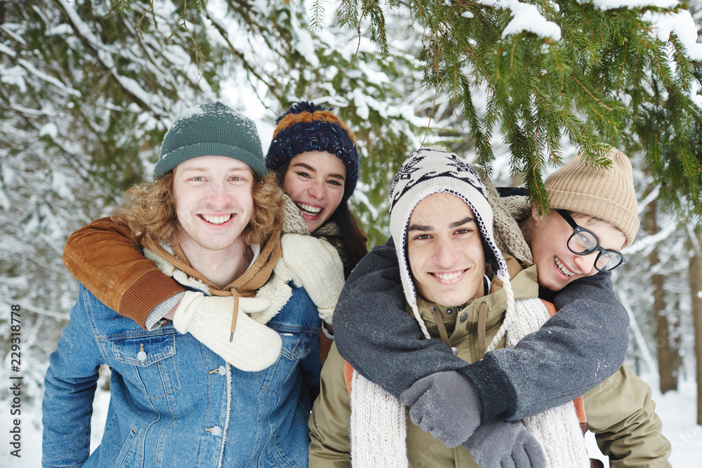 Portrait of two beautiful young couples having fun on winter resort and smiling at camera while posing in snowy forest Portrait of two beautiful young couples having fun on winter resort and smiling at camera while posing in snowy forest
