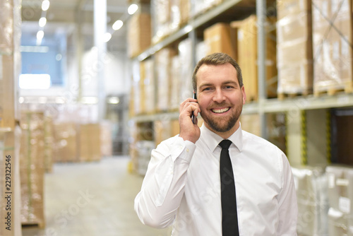 Happy businessman makes a phone call in the warehouse of a logistics company // fröhlicher Geschäftsmann telefoniert im Lager einer Logistik-Firma photo