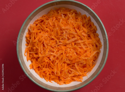Close-up view of grated carrot is in round bowl.