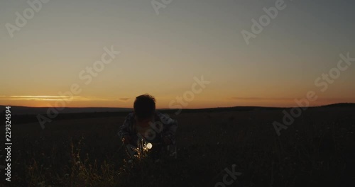 Three years boy at sunset playing with a flashlight through the grass. photo