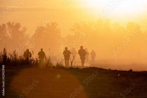 silhouette action soldiers walking hold weapons the background is smoke and sunset. War, military and danger concept