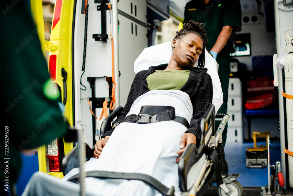 Paramedics moving a patient on a stretcher into an ambulance - obrazy, fototapety, plakaty 