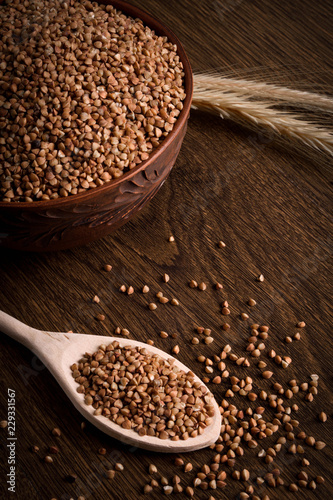 Buckwheat in a wooden bowl on a wooden background near the ears of wheat. wooden spoon with Buckwheat © Ivan