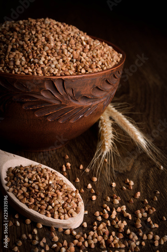 Buckwheat in a wooden bowl on a wooden background near the ears of wheat. wooden spoon with Buckwheat