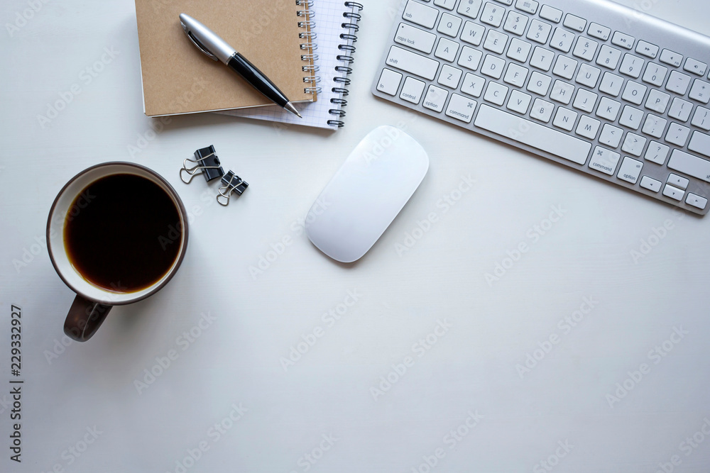 White wooden table with keyboard, mouse, pen, notebook, document clips and a cup of coffee. Workspace top view with copy space. White wooden table with keyboard, mouse, pen, notebook, document clips and a cup of coffee. Workspace top view with copy space.