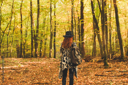 Girl of redheads in knitted ethnic ponchos, trousers and a backpack. The warming of the atmosphere is warm and the sun.Portret in the forest. Natural background. Woman travels Travel the photo.
