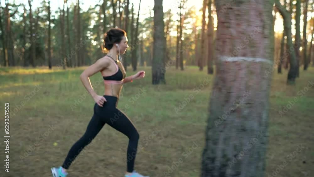 Close up of woman with headphones running through an autumn forest at sunset Close up of woman with headphones running through an autumn forest at sunset