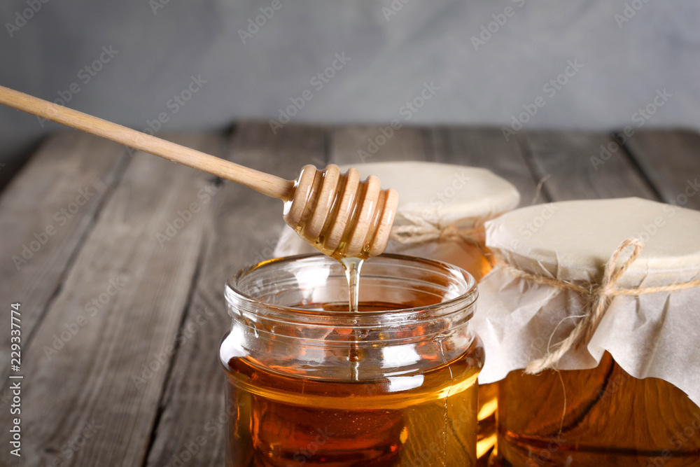 Pouring aromatic honey into jar, closeup. Honey in glass jars and honeycombs wax on wooden background. Wooden stick , instruments Pouring aromatic honey into jar, closeup. Honey in glass jars and honeycombs wax on wooden background. Wooden stick , instruments