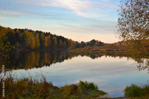 Dawn in the forest near the lake. The forest is reflected in the water. Autumn Early morning. Russia