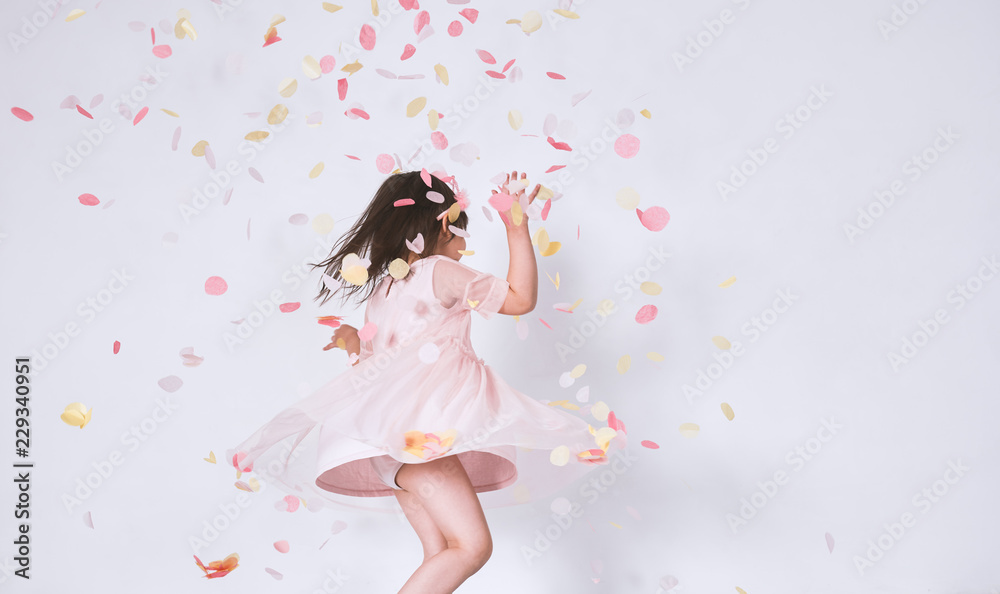 Cheerful cute little girl wearing pink dress in tulle with princess crown dancing on confetti surprise isolated on white studio wall. Playful toddler girl celebrating her birthday party having fun Cheerful cute little girl wearing pink dress in tulle with princess crown dancing on confetti surprise isolated on white studio wall. Playful toddler girl celebrating her birthday party having fun