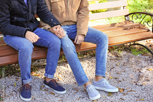 Happy gay couple holding hands while sitting on bench in park