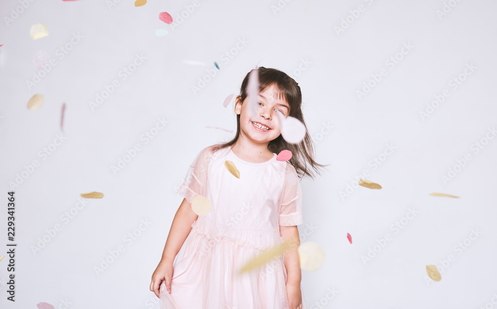 Cute little girl wearing pink dress in tulle with princess crown dancing on confetti surprise isolated on white studio wall background. Playful toddler girl celebrating her birthday party having fun Cute little girl wearing pink dress in tulle with princess crown dancing on confetti surprise isolated on white studio wall background. Playful toddler girl celebrating her birthday party having fun