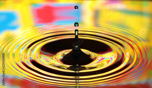 Water drops splash. Yellow colored ripples, reflections on water surface