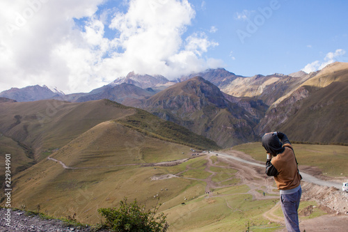 Young curly traveler taking photo with camera in Kazbegi.