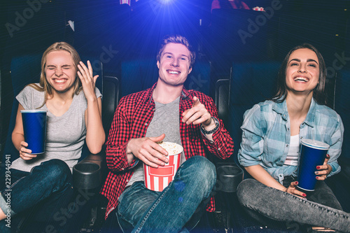 Beautiful picture of happy people laughing in ciname hall. They are looking on screen and smiling. Girls and guy look absolutely stunning and happy.