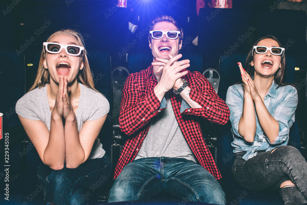 Happy and delightful people are sitting together and watching movie with pleasure. Each of them are keeping their hands together. They are excited. Happy and delightful people are sitting together and watching movie with pleasure. Each of them are keeping their hands together. They are excited.