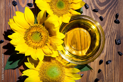 Fototapeta Naklejka Na Ścianę i Meble -  Top view of three yellow sunflowers and oil in bowl with black seeds around on wooden background