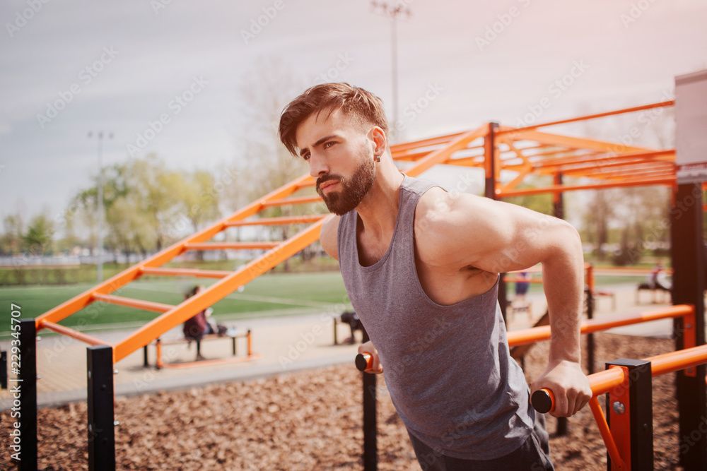 Well-built brunette is doing some push-ups using horizontal bar. Man is looking straight forward. He is very serious. Well-built brunette is doing some push-ups using horizontal bar. Man is looking straight forward. He is very serious.
